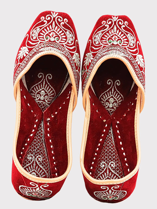 Pair of red embroidered shoes with intricate white patterns on a light gray background